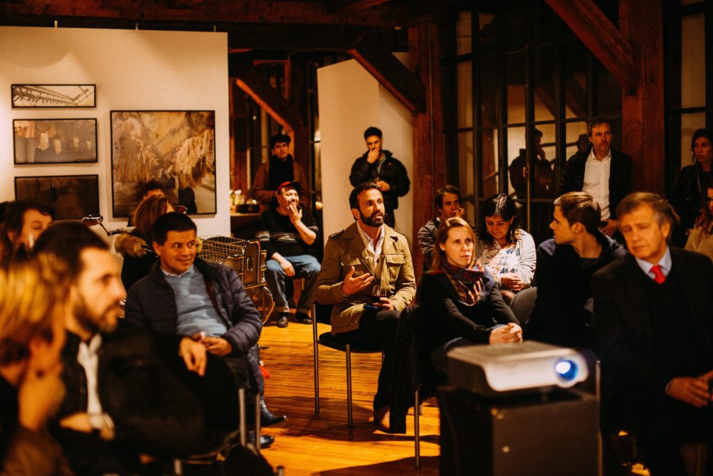  People seated in a gallery, watching a presentation.