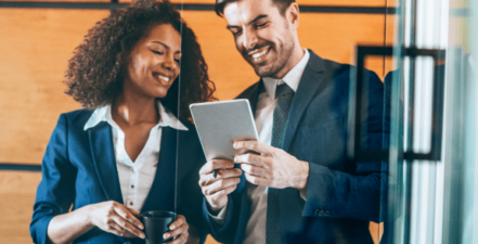 Two office workers smiling and looking at tablet.