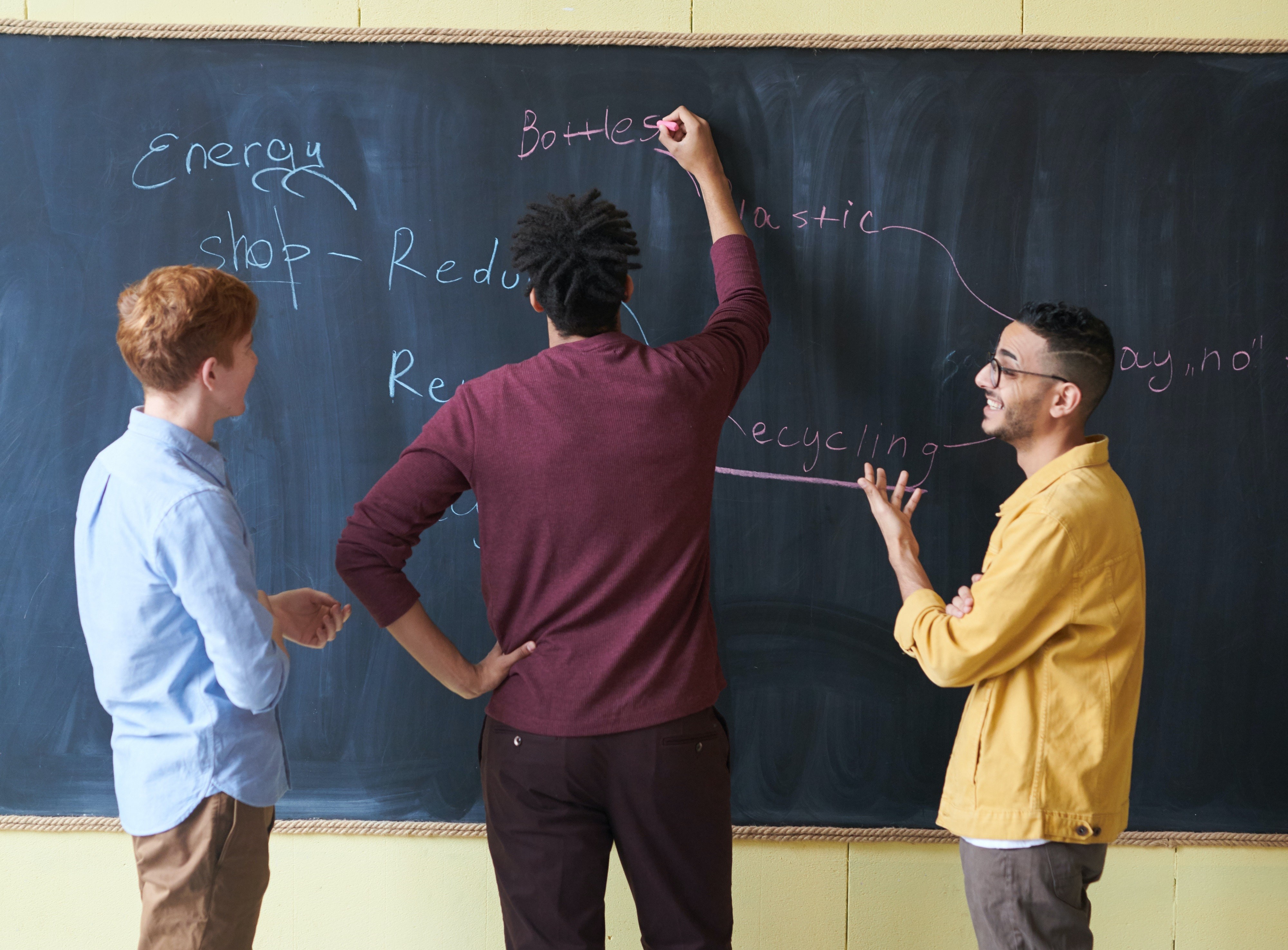 Three men stand facing a blackboard, brainstorming energy-related topics.