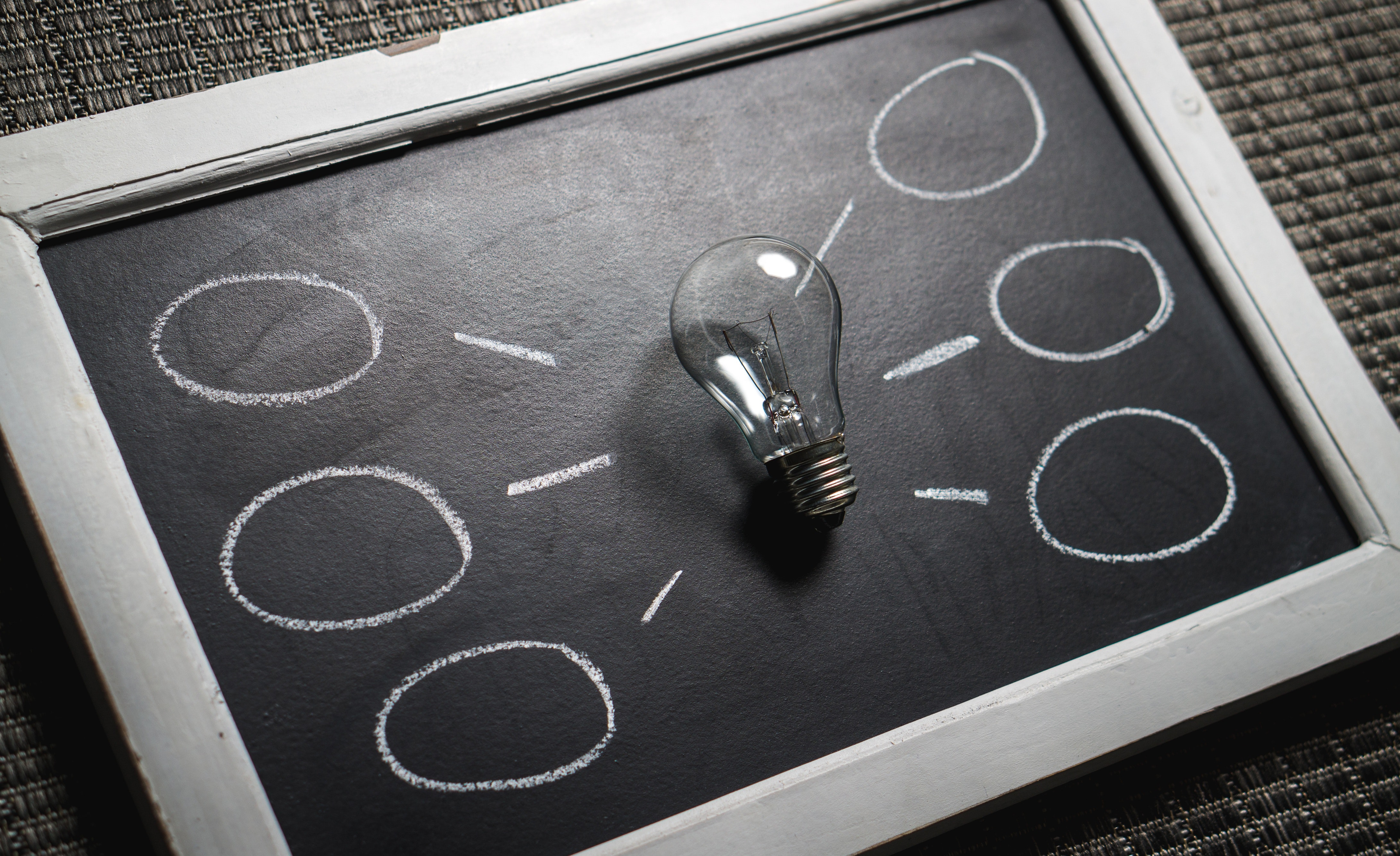 A lightbulb resting on a chalkboard with six bubbles drawn in chalk coming off it.