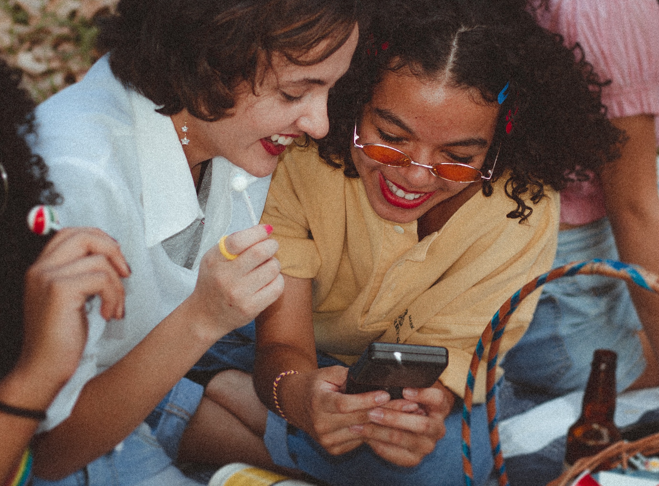  Two young women look down at a phone, smiling and laughing.