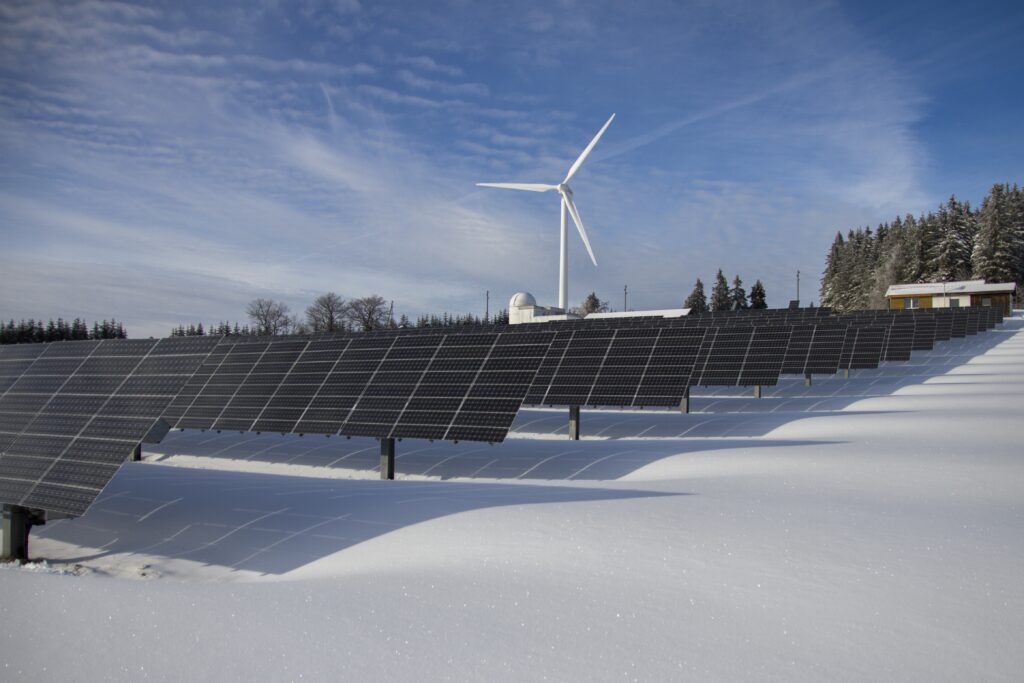 Solar panels in a snowy field, with a wind turbine in the background.