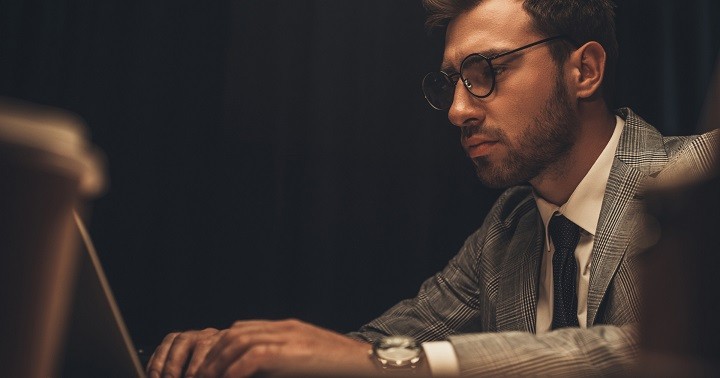 A man wearing a watch and suit types intently on a keyboard.