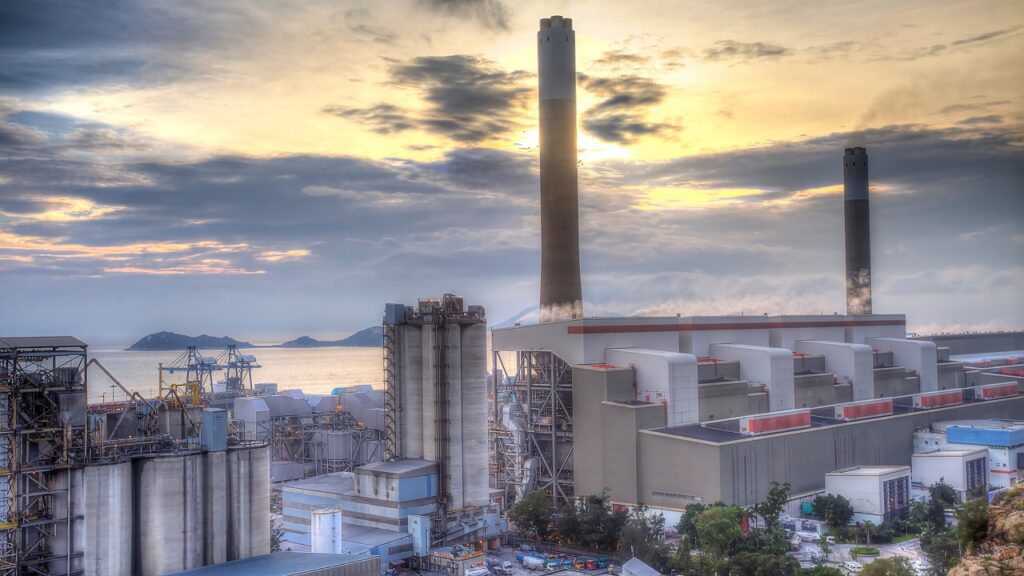 Image of factory beside the ocean with large chimneys.