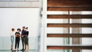 Group of people standing together in discussion in a foyer with a set of stairs in the foreground.