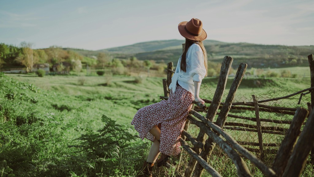 Photo of a woman leaning against a fence in a rural area.