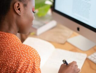 Person sitting at a computer writing a list.