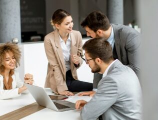 Four people sitting or standing at a table, discussing stakeholder requirements for a project.