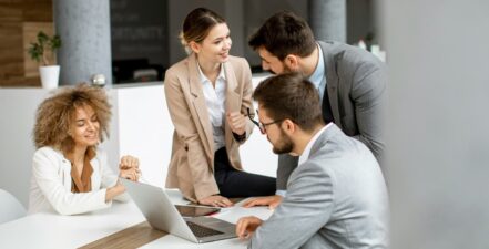 Four people sitting or standing at a table, discussing stakeholder requirements for a project.