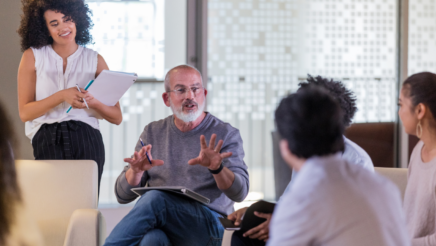 People in a meeting with a man explaining things to a group