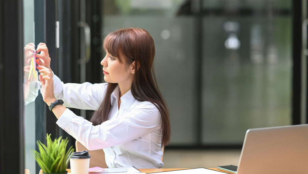 Woman using sticky notes to organize information on a window.