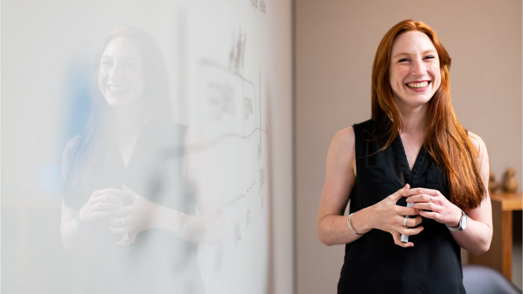 Woman smiling in front of a whiteboard.