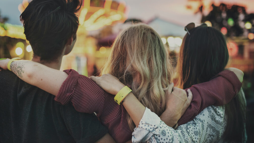Three people with their arms around each other at a community event. To represent community engagement plan.