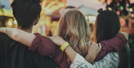 Three people with their arms around each other at a community event. To represent community engagement plan.