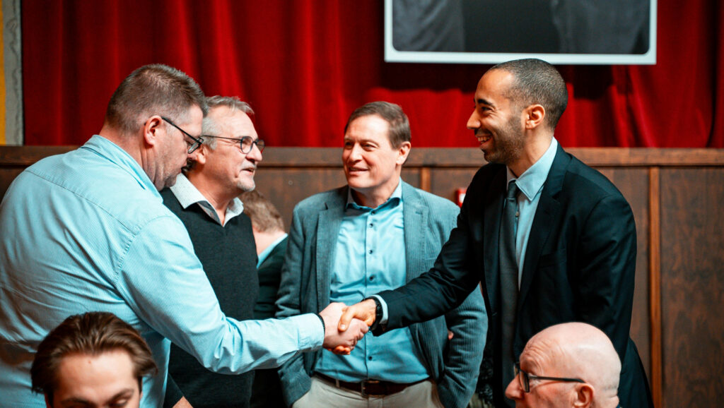 Five men in formal attire. Two are shaking hands - to represent meeting local government representatives