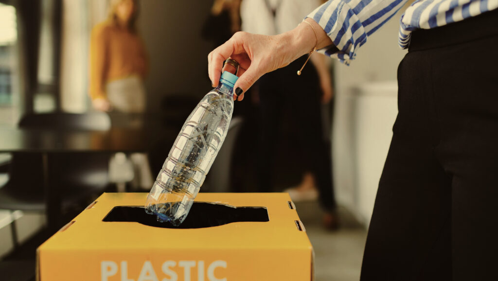Person in an office putting a plastic bottle in a recycling bin.