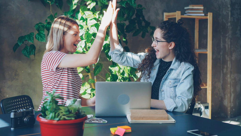 Two female work colleagues high-fiving to represent positive ESG reputations.