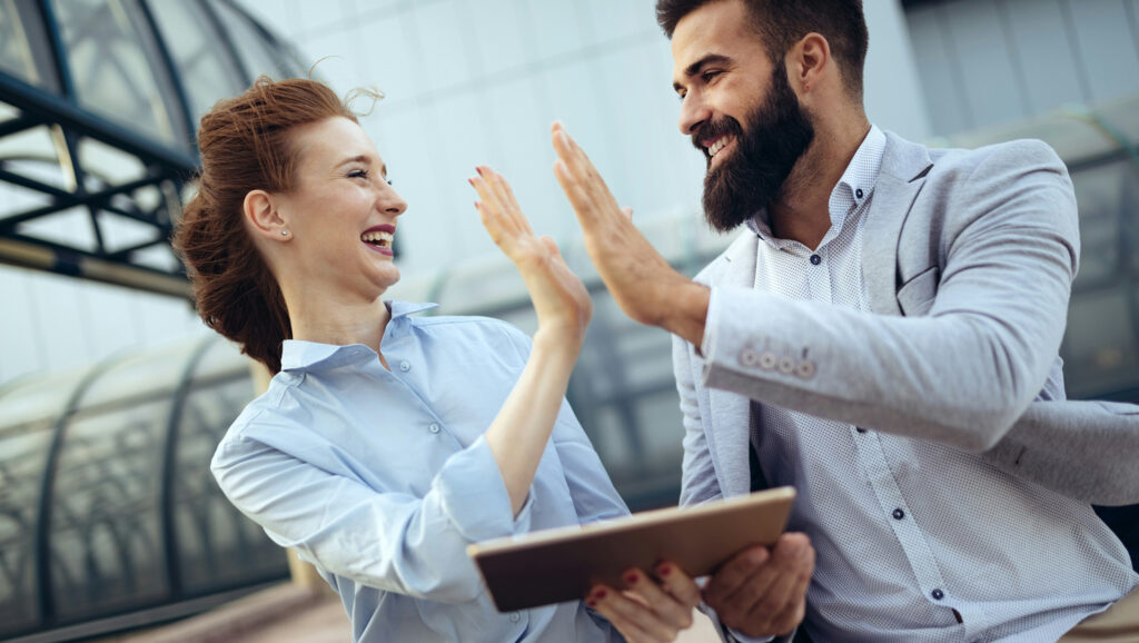 A male and a female, business people, high fiving to represent successfully setting stakeholder goals.