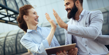 A male and a female, business people, high fiving to represent successfully setting stakeholder goals.